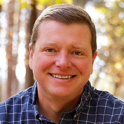Chris Short Headshot (Chris in his office with canvas panels picturing Detroit in background)